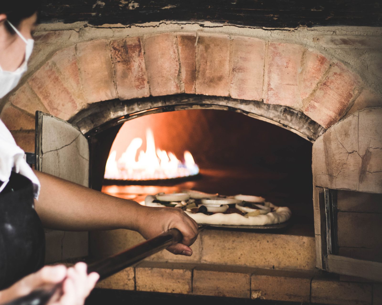 Un pizzaïolo enfourne une pizza dans un four à bois en briques