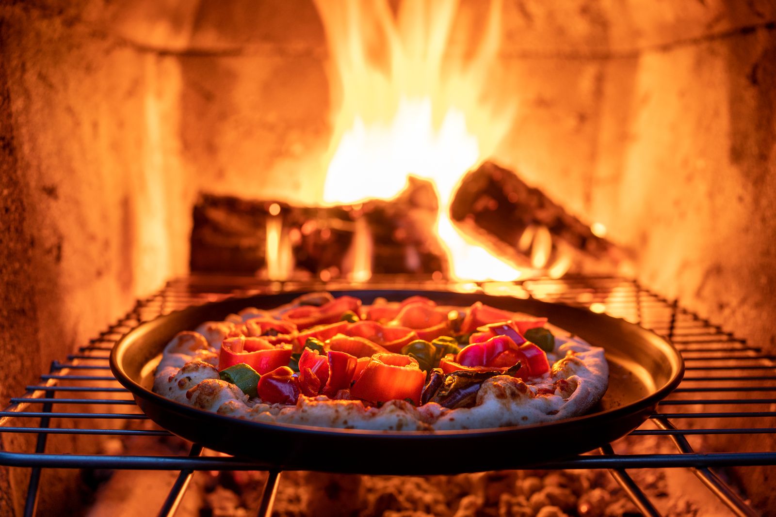 Une pizza garnie posée près des braises