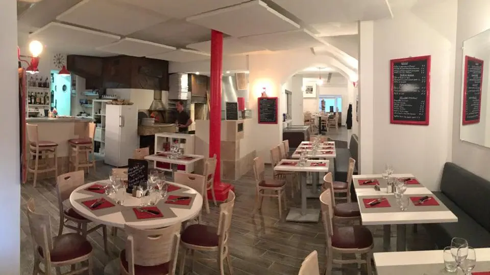 La salle du restaurant : poteau rouge, ardoises encadrées de rouge et tables dressées