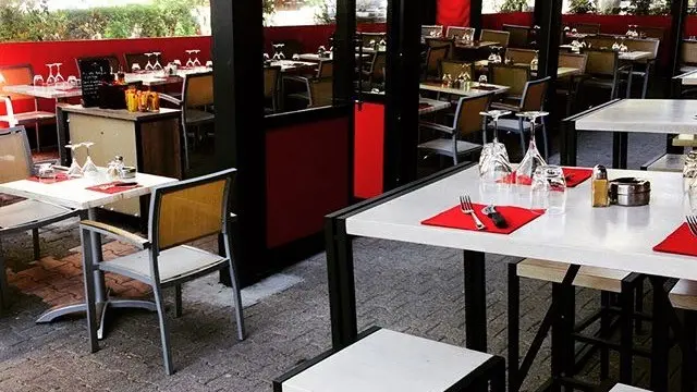 Terrasse : tables blanches, sets de table rouges, verres en place