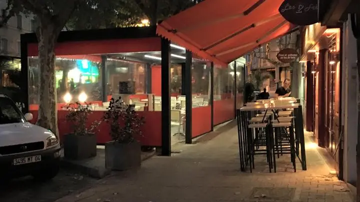 La terrasse sous l'auvent rouge, de nuit, avec des tables hautes